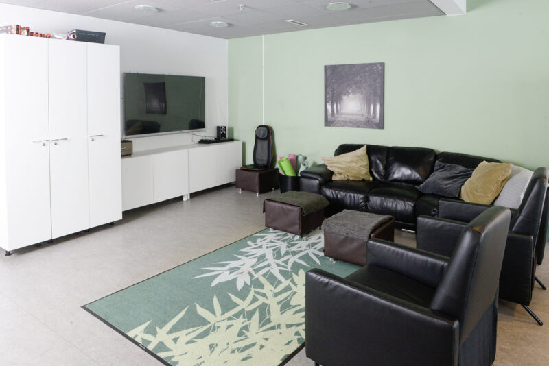 Oleskelutilassa mustia nahkasohvia, tv-taso ja televisio. Seinät ovat vaaleanvihreän väriset, lattialla vihertävä matto.