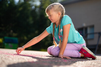 Tyttö istuu polvilleen asfaltilla ja piirtää liidulla maahan.