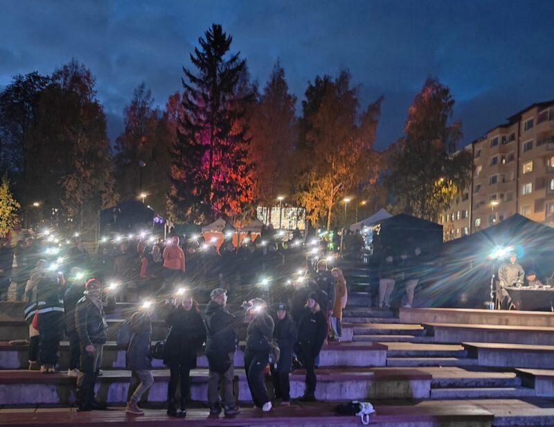 Ihmisiä hämärässä ulkona lamput käsissään.