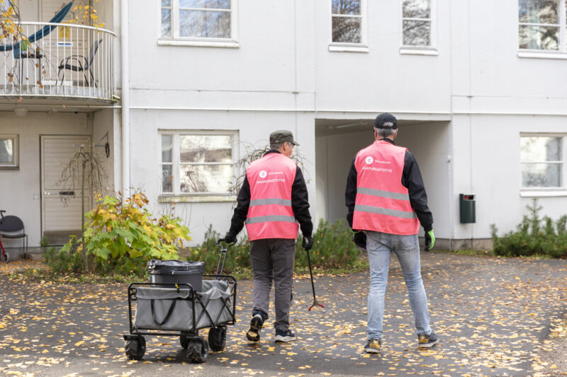 Kaksi miestä kuvattuna ulkona takaapäin, molemmilla pinkki huomioliivi.